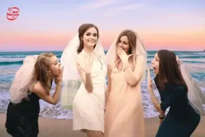 group of four women celebrating a bachelorette party on the beach at sunset. The bride, wearing a white dress and veil, proudly shows her engagement ring while her friends, also wearing veils, react with excitement and laughter.